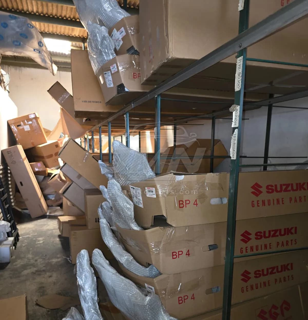 Suzuki Genuine Parts bumper cartons stacked in the body-parts section of the warehouse