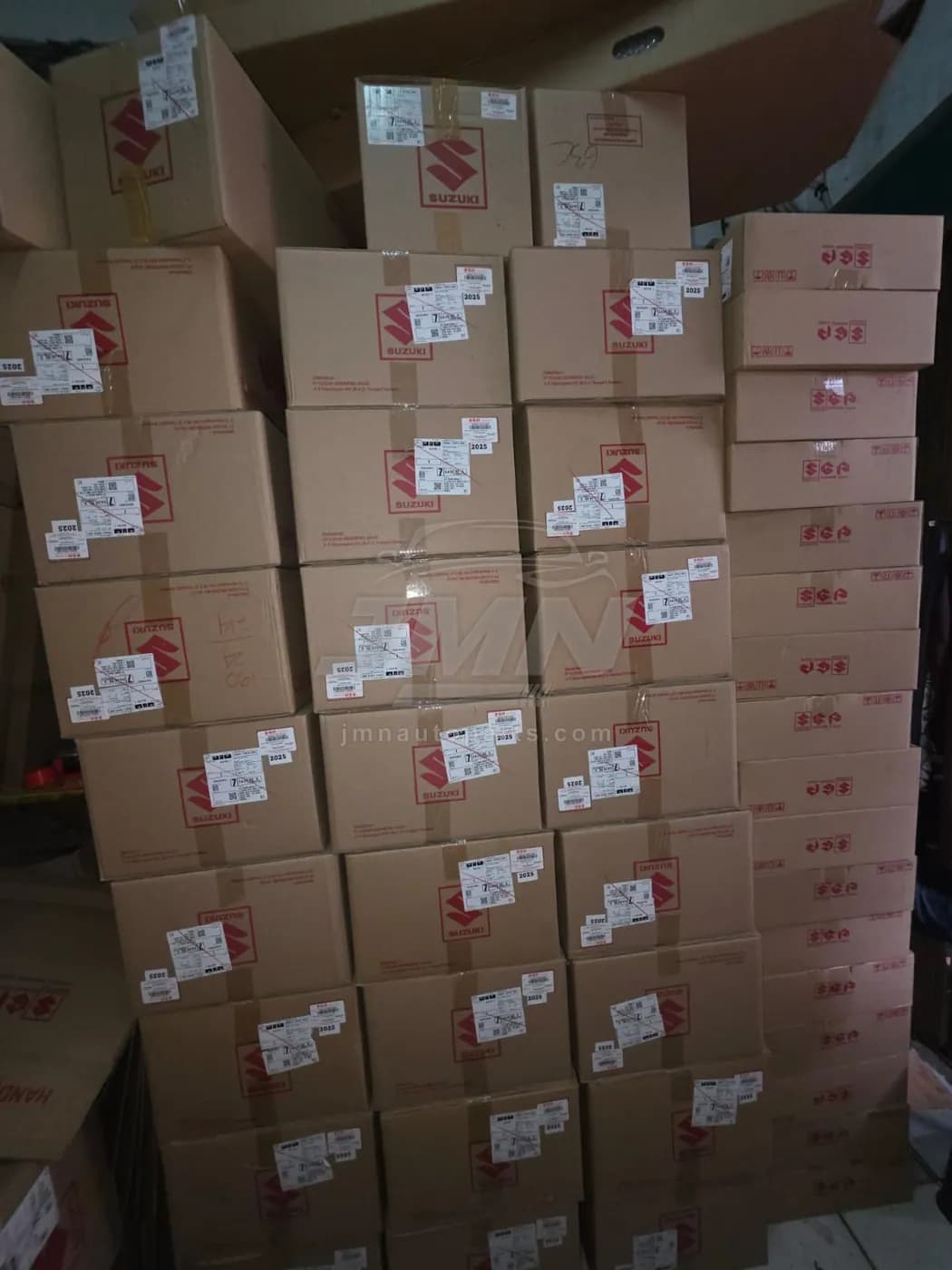 Sealed Suzuki Genuine Parts cartons stacked in the JMN warehouse, each with a 2025 batch label